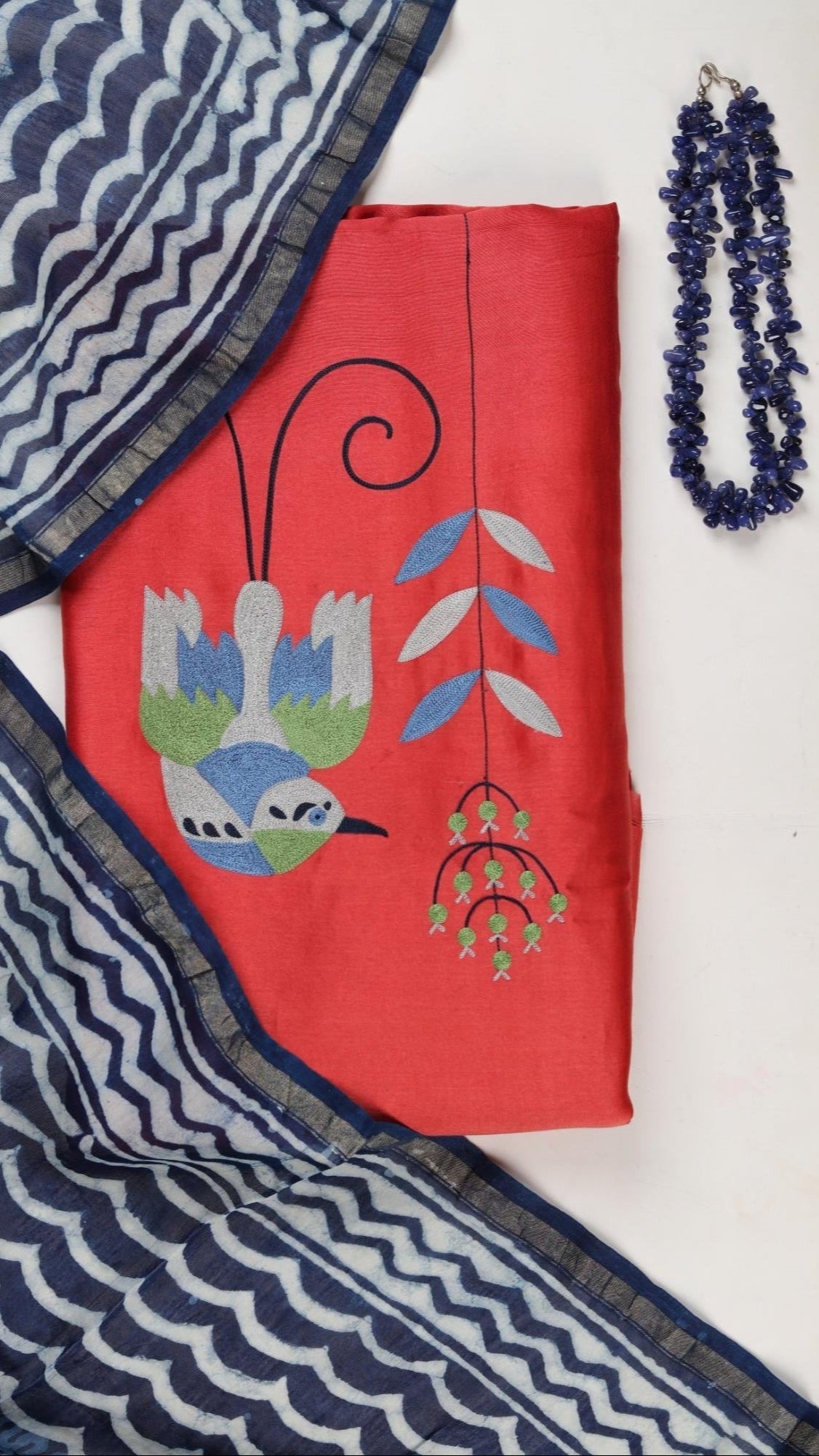 Red fabric with bird design, blue and white patterned fabric, and necklace on a white background